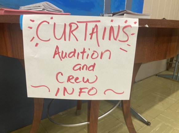 a sign announcing the musical and information is placed on a table outside of Mrs. Findleys room.